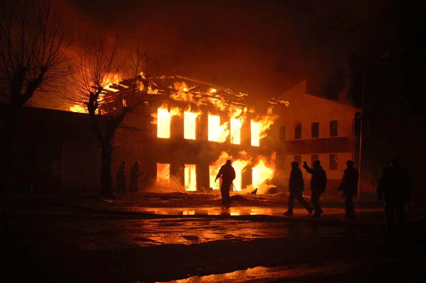 A building engulfed in flames at night, with firefighters silhouetted in front