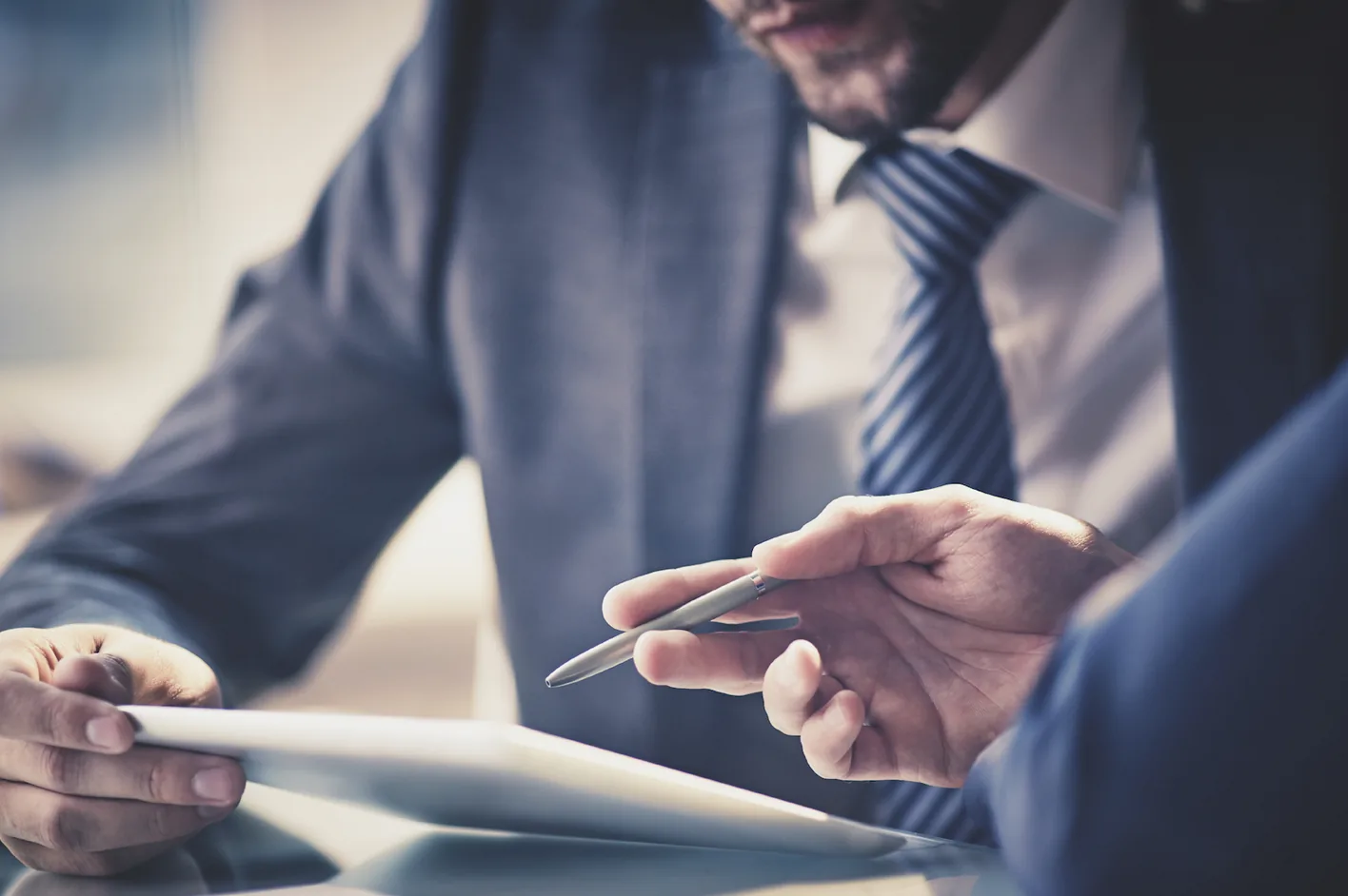 A man in a suit pointing a pen at a tablet during a meeting