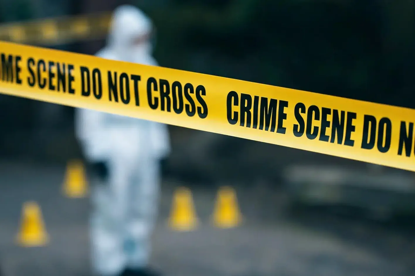 Crime scene tape, with a forensic investigator and evidence markers behind it