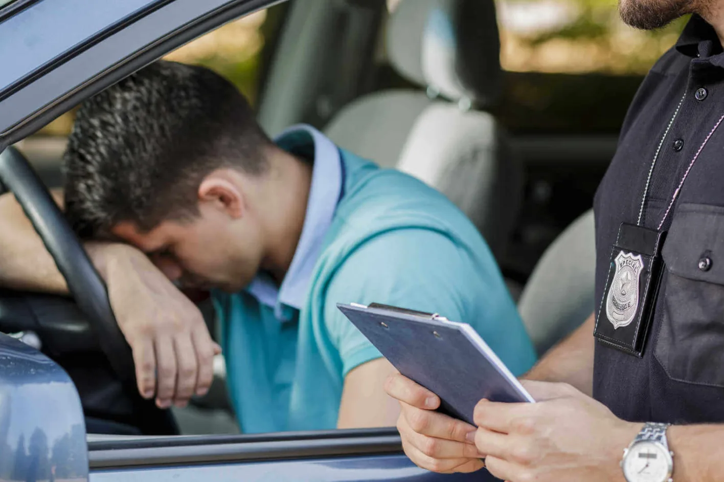 A driver resting his head on the steering wheel as an officer writes on a clipboard