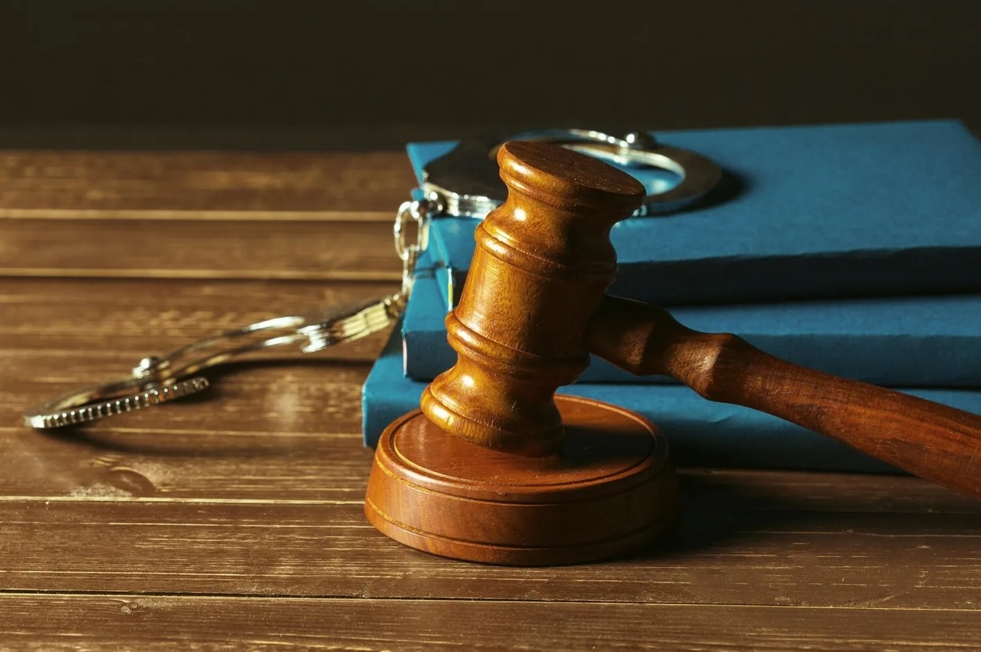 A judge's gavel and handcuffs on law books on a wooden desk