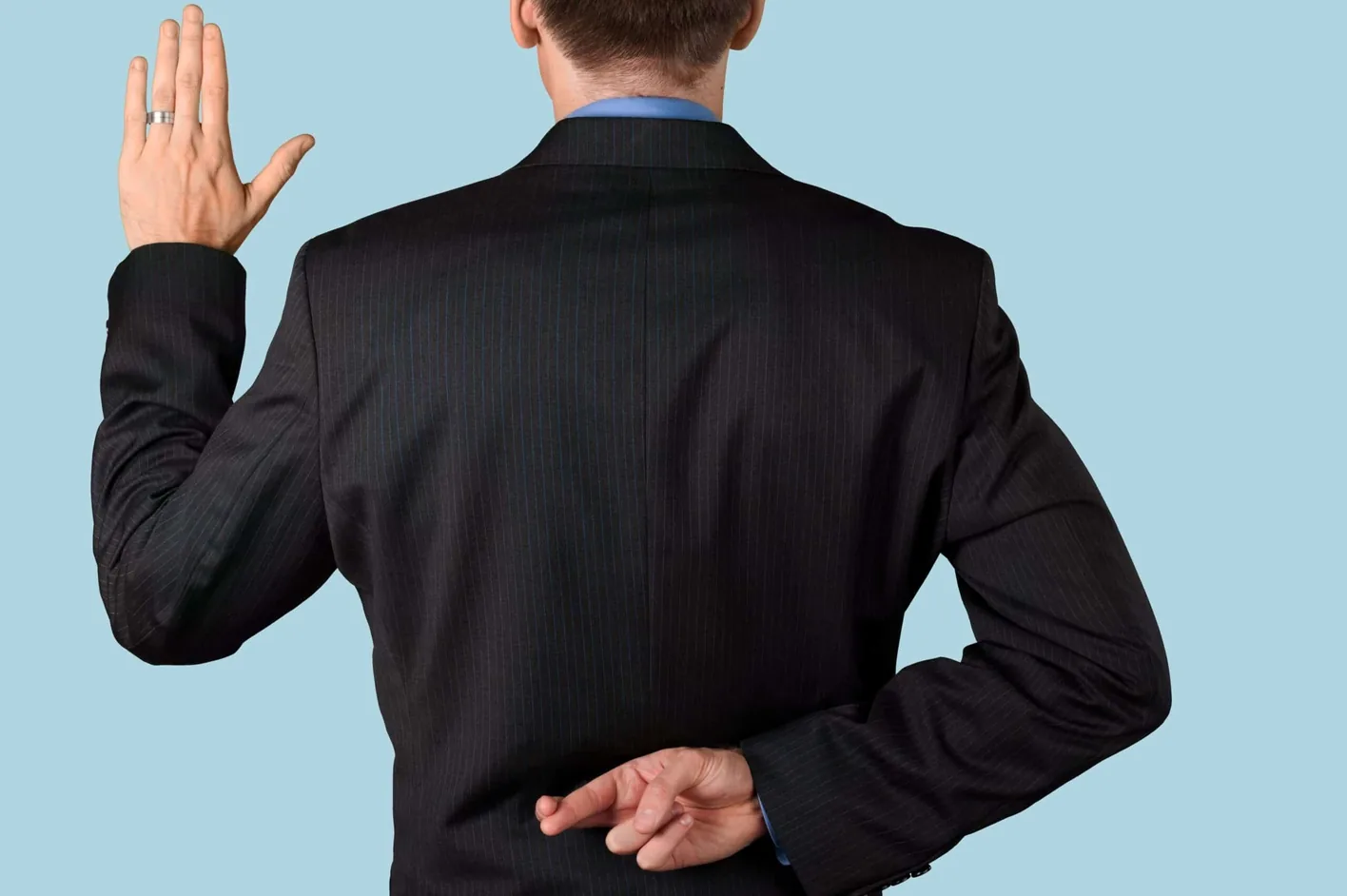 A man raising his right hand to take an oath while crossing his fingers behind his back