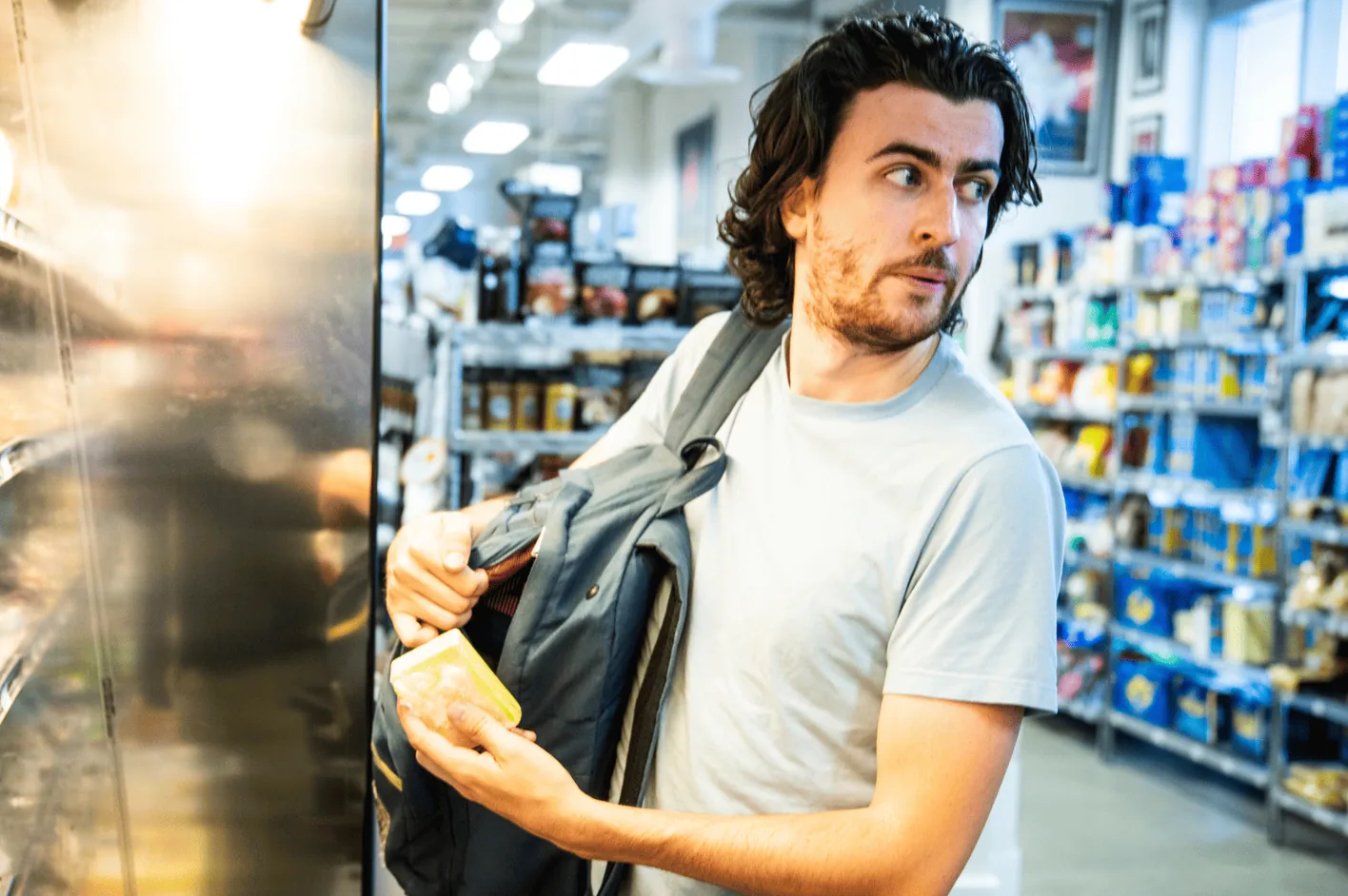 A man glancing over his shoulder as he slips an item into his bag in a store