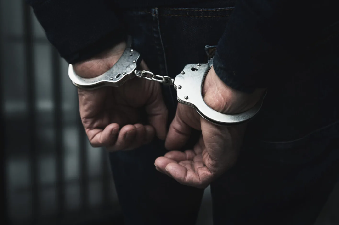 A man in handcuffs, his hands behind his back, in a dark room