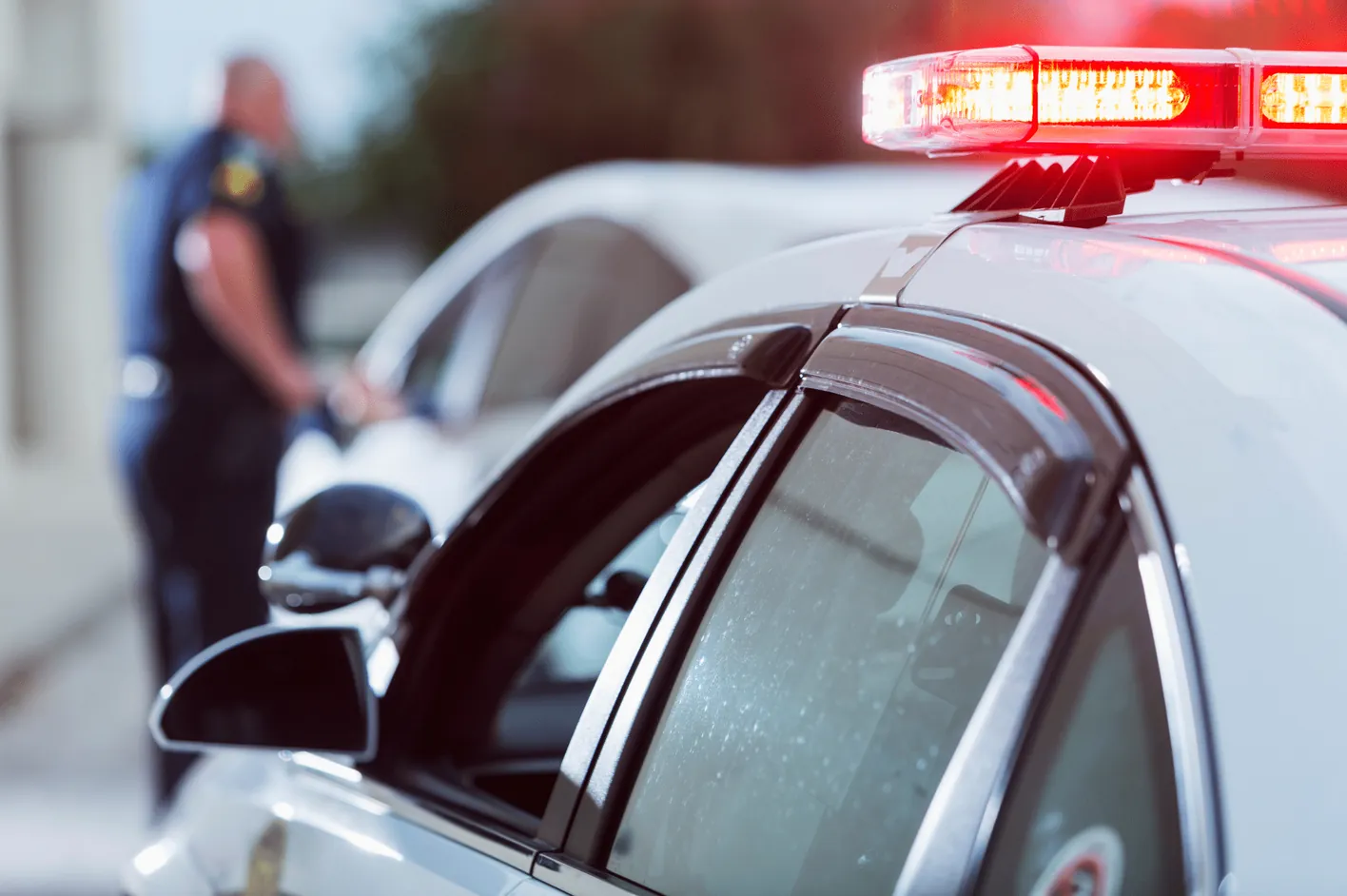 A police officer standing beside a patrol car with its lights flashing