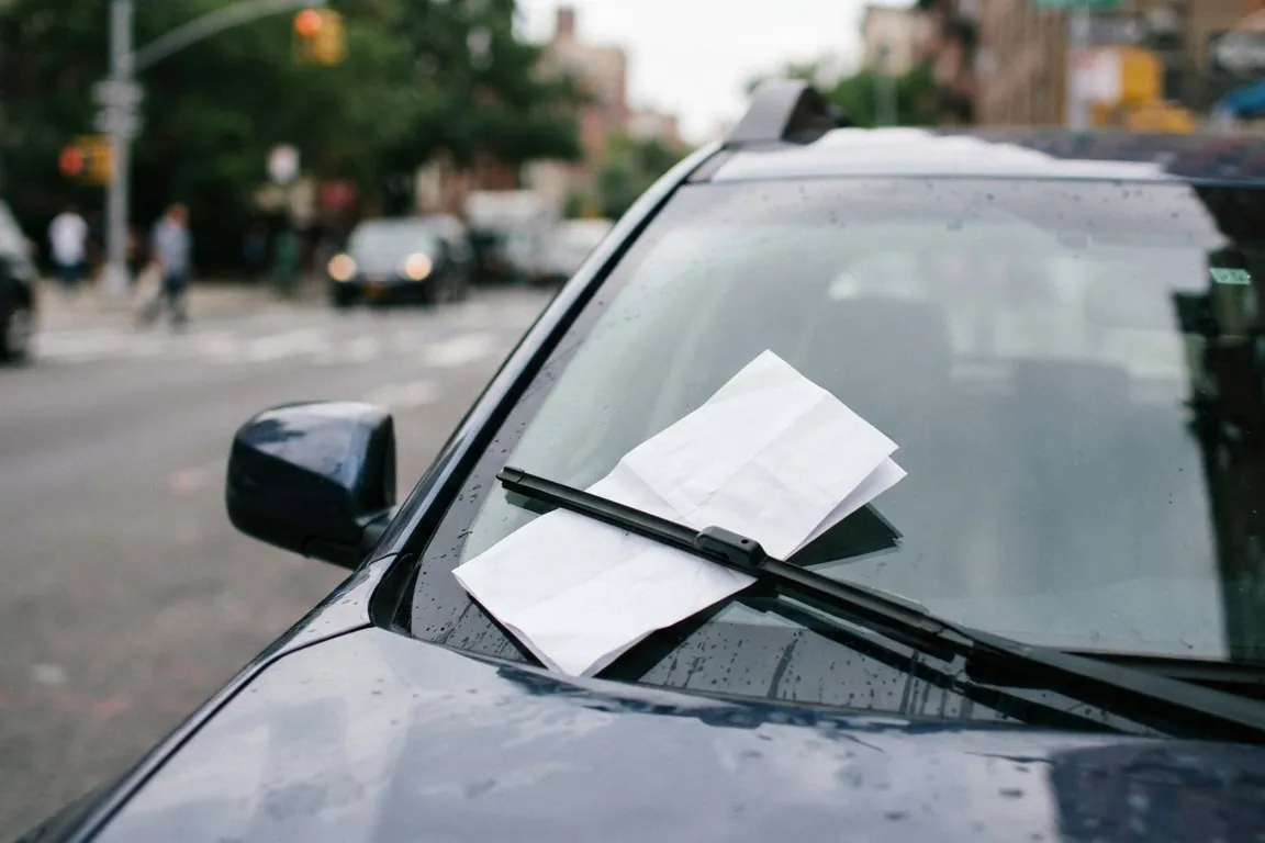 A folded paper citation tucked under a car's windshield wiper, the street behind soft and out of focus