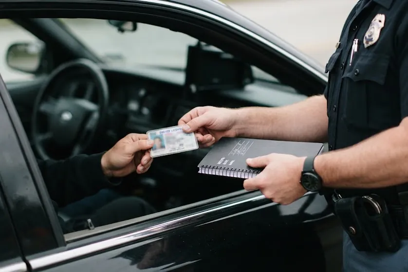A driver handing a license to a police officer through the car window