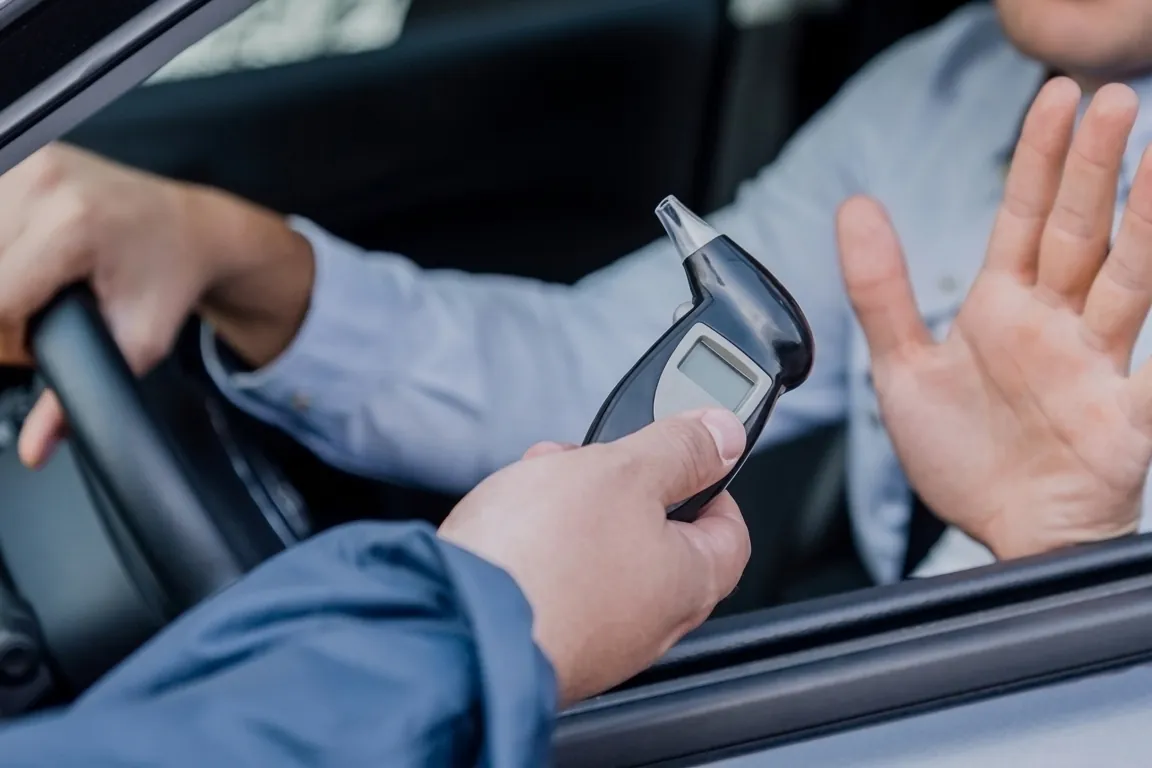 A driver raising a hand to refuse a breath-test device held to the car window